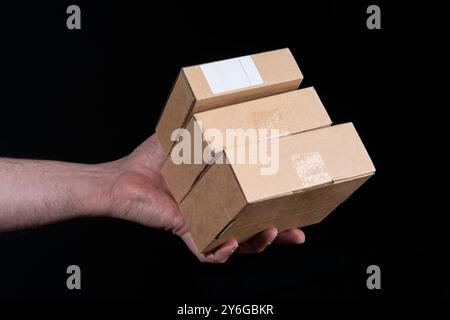 Nahaufnahme der Hand eines Mannes, der drei kleine Wellpappkartons vor schwarzem Hintergrund hält Stockfoto