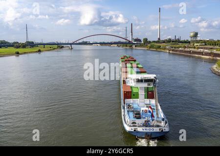 Das mit Containern beladene holländische Frachtschiff Vrido auf dem Rhein bei Duisburg, das hinter der sogenannten Solidaritätsbrücke über den Rhein hinabfährt; Stockfoto