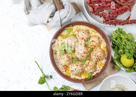 Essen, Essen, CRABMEATBALLS Krabben-Fleischbällchen in weißer cremiger Sauce in roter Pfanne, ganze Königskrabbe, Koriander, Zitrone und Weißwein auf weißem Hintergrund Stockfoto