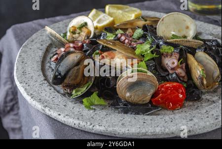 Essen, Meeresfrüchte, schwarze Fettuccine Fehttuchini. Schwarze Nudeln mit Tintenfischen, Tintenfischmuscheln, Muscheln auf Steinplatte. Gourmet-Gericht Stockfoto