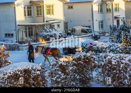 Pferdeschlitten mit Weihnachtsmann, der Weihnachtsgeschenke in der verschneiten Nachbarschaft liefert. Stockfoto