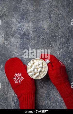 Essen, Weihnachten und Neujahr gemütliche Feiertagskomposition mit Schal, Frauenhänden in Fäustlingen, Tassen mit heißem Getränk und Marshmallow auf dem grauen Beton bac Stockfoto