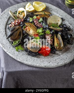 Essen, Meeresfrüchte, schwarze Fettuccine Fehttuchini. Schwarze Nudeln mit Tintenfischen, Tintenfischmuscheln, Muscheln auf Steinplatte. Gourmet-Gericht Stockfoto