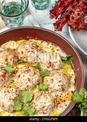 Essen, Essen, CRABMEATBALLS Krabben-Fleischbällchen in weißer cremiger Sauce in roter Pfanne, ganze Königskrabbe, Koriander, Zitrone und Weißwein auf weißem Hintergrund Stockfoto