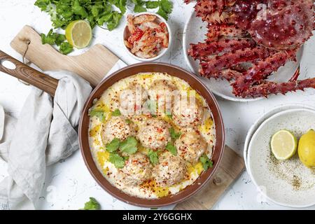 Essen, Krabben-Fleischbällchen in weißer cremiger Sauce in roter Pfanne, ganze Königskrabbe, Koriander, Zitrone und Weißwein auf weißem Hintergrund Stockfoto