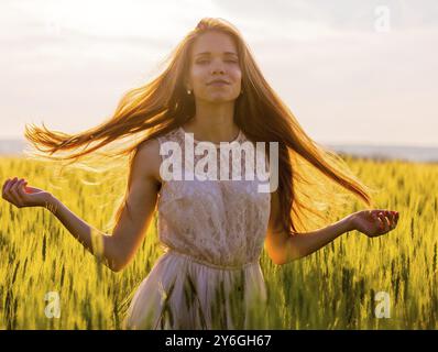 Schönes Mädchen in einem Weizenfeld mit fließenden Haaren, beleuchtet vom Licht der untergehenden Sonne Stockfoto