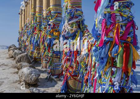 Hölzerne Ritualsäulen mit bunten Bändern und Schamanenfelsen, einer der heiligen Orte im gefrorenen Baikalsee in der Wintersaison Sibiriens, Russlands, Europas Stockfoto