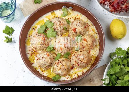 Essen, Krabben-Fleischbällchen in weißer cremiger Sauce in roter Pfanne, ganze Königskrabbe, Koriander, Zitrone und Weißwein auf weißem Hintergrund Stockfoto