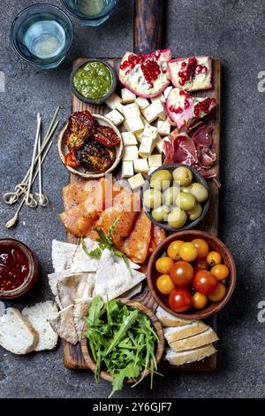 Essen, Essen, Antipasto. Weinset Vorspeise. Schinken serrano, Räucherlachs, getrocknete und frische Tomaten, Olivenkäse, Wein an Bord. Draufsicht, graue Cncrete-Ba Stockfoto