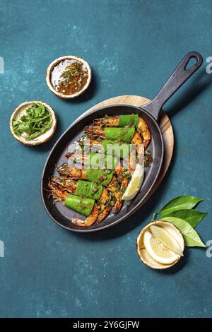 Essen, Essen, scharfe Knoblauch Tigergarnelen auf Pfanne mit Zitronenblättern auf blauem Backboden, Blick von oben Stockfoto
