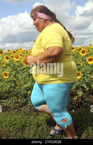 Fitness, übergewichtige Frau, die auf einem Sonnenblumenfeld läuft Stockfoto