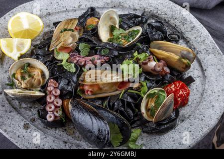 Essen, Meeresfrüchte, schwarze Fettuccine Fehttuchini. Schwarze Nudeln mit Tintenfischen, Tintenfischmuscheln, Muscheln auf Steinplatte. Gourmet-Gericht Stockfoto