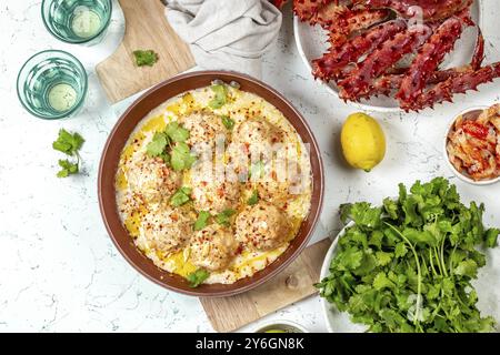 Essen, Essen, CRABMEATBALLS Krabben-Fleischbällchen in weißer cremiger Sauce in roter Pfanne, ganze Königskrabbe, Koriander, Zitrone und Weißwein auf weißem Hintergrund Stockfoto