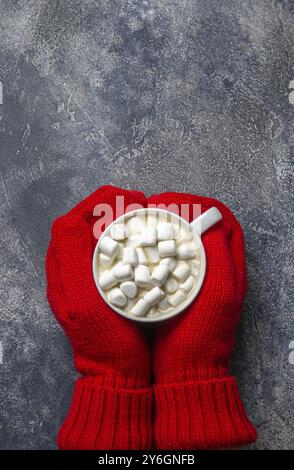 Essen, Essen, Weihnachten und Neujahr gemütliche Feiertagskomposition mit Schal, Frauenhänden in Handschuhen, Tassen mit Heißgetränk und Marshmallow auf dem grauen Conre Stockfoto