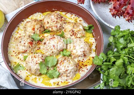 Essen, Krabben-Fleischbällchen in weißer cremiger Sauce in roter Pfanne, ganze Königskrabbe, Koriander, Zitrone und Weißwein auf weißem Hintergrund Stockfoto