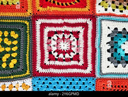 Fragment einer Decke aus Granny Square, gehäkelt mit rotem, weißem, gelbem, grünem, blauem und orangenem Garn mit verschiedenen Motiven. Stockfoto