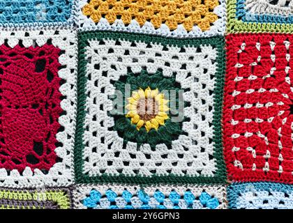 Fragment einer Decke aus Granny Square, gehäkelt mit rotem, weißem, gelbem, grünem, blauem und orangenem Garn mit verschiedenen Motiven. Stockfoto