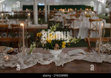 Eleganter Hochzeitsempfang mit Blumenaufsatz, Kerzen und ordentlich angeordnetem Geschirr in einem wunderschön eingerichteten Veranstaltungsraum. Stockfoto