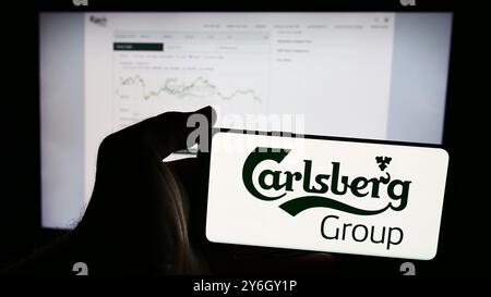 In dieser Abbildung hält eine Person ein Mobiltelefon mit dem Logo der dänischen Brauerei Carlsberg WIE vor der Webseite. Stockfoto