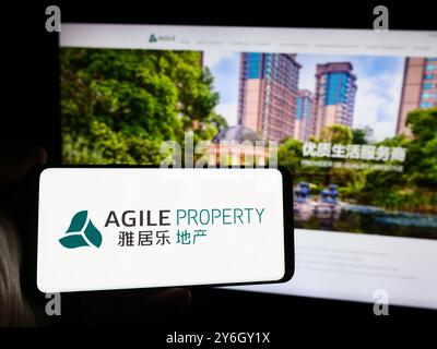 In dieser Abbildung hält eine Person ein Smartphone mit dem Logo des chinesischen Unternehmens Agile Property Holdings Limited vor der Website. Stockfoto