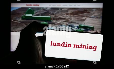 In dieser Abbildung hält eine Person ein Mobiltelefon mit dem Logo des kanadischen Unternehmens Lundin Mining Corporation vor der Unternehmenswebsite. Stockfoto