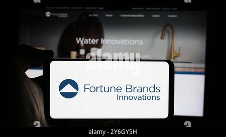 In dieser Abbildung hält eine Person ein Mobiltelefon mit dem Logo des amerikanischen Sicherheitsunternehmens Fortune Brands Innovations Inc. Vor der Webseite. Stockfoto