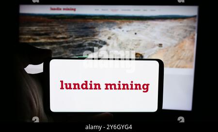 In dieser Abbildung hält eine Person ein Handy mit dem Logo des kanadischen Unternehmens Lundin Mining Corporation vor der Webseite. Stockfoto