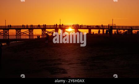 Silhouette der Menschen bei Sonnenuntergang am Pier an einem goldenen Sommerhimmel. Stockfoto