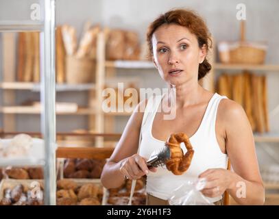 Frau packt Croissant in Plastiktüte in der Bäckerei Stockfoto