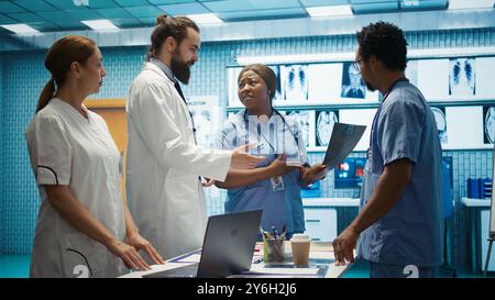 Das Klinikteam untersucht Röntgenstrahlen und diskutiert die Behandlungsstrategie in einem medizinischen Schrank. Arzte mit Expertise in Radiologie und Krankheitsprävention, die kollektive Arbeit für den Gesundheitsdienst leisten. Kamera B.. Stockfoto