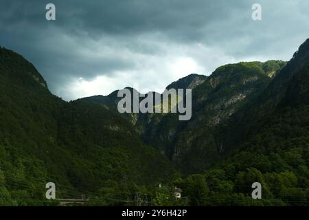 Dramatische Wolkenformationen schweben über majestätischen Bergen, während das letzte Licht des Tages üppige grüne Täler erleuchtet und einen atemberaubenden Kontrast in der e schafft Stockfoto