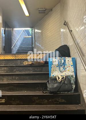 New York City ist übersät mit nicht untergebrachten Obdachlosen, die scheinen zu schlafen, wo immer sie können, wie dieser Mann auf den Stufen einer U-Bahn-Station am Bryant Park in Midtown Manhattan. Stockfoto