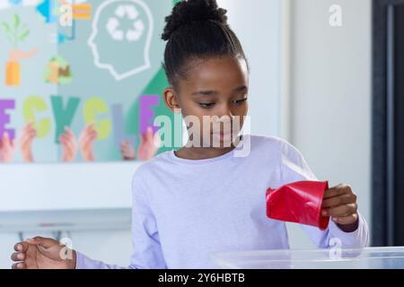 Recycling in der Schule legte ein afroamerikanisches Mädchen rotes Papier in den Recyclingbehälter und konzentrierte sich auf die Aufgabe Stockfoto