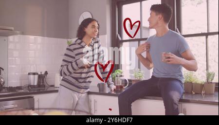 Bild von roten Herzen über glückliche, verschiedene schwule männliche Paare, die in der Küche reden und lachen Stockfoto