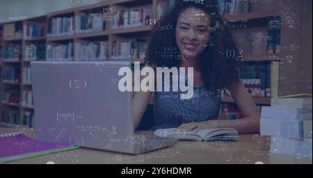 Bild mathematischer Gleichungen über glückliche birassische Studentin mit Laptop in Bibliothek Stockfoto