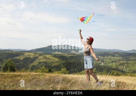 Lächelnde Frau, die Drachen auf dem Feld unter blauem Himmel fliegt. Leerzeichen für Text Stockfoto