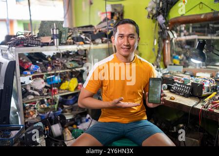 Der asiatische Elektroreparateur lächelt, als er einen Handybildschirm zeigt Stockfoto