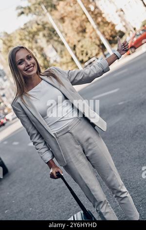 Taxi! Schöne junge Frau im Anzug, die eine Fahrt feiert und lächelt, während sie draußen steht Stockfoto