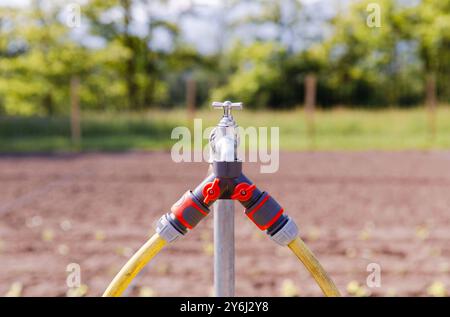 Schläuche, die mit einem Wasserhahn in einem Garten mit verschwommenem Hintergrund verbunden sind, landwirtschaftliche Bewässerungsanlage, Konzept zur Landwirtschaft Stockfoto