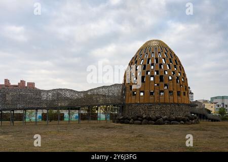 Eine einzigartige architektonische Struktur, die einem Ei ähnelt, mit Gitterdesign, vor einem bewölkten Himmel in einem städtischen Gebiet. Stockfoto