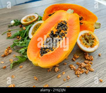 Papaya-Frucht, Passionsfrucht, Rucola und Müsli auf hellem hölzernem Hintergrund. Scheiben süßer Papaya, Maracuja, grüner Rucola umgeben von Granola fla Stockfoto