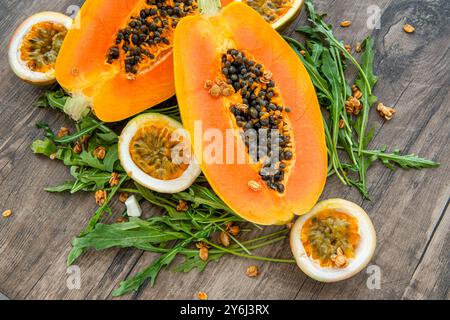 Papaya, Passionsfrucht, Rucola und Müsli auf dunklem hölzernem Hintergrund. Scheiben von süßer Papaya, Passionsfrucht und Rucola umgeben von Granola-Flocken o Stockfoto