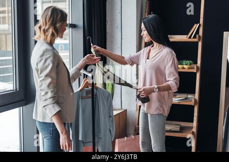 Du solltest es anprobieren. Schöne junge Frau, die ihrem Kunden bei der Auswahl von Kleidung hilft, während sie in der Modeboutique arbeitet Stockfoto