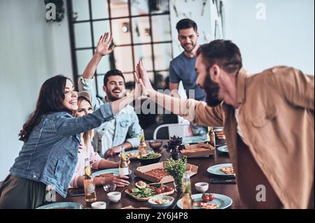 High-Five! Junge Mann und Frau geben sich gegenseitig High-Five, während sie ein Abendessen mit Freunden genießen Stockfoto
