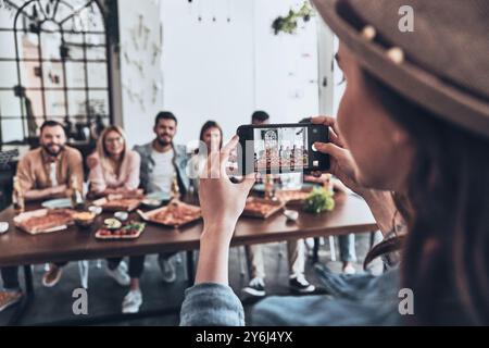 Glückliche Erinnerungen schaffen. Eine junge Frau fotografiert eine Gruppe ihrer Freunde mit dem Smartphone, während sie eine Dinnerparty feiern Stockfoto
