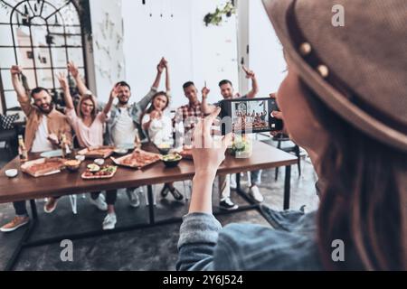 Zusammen verrückt werden. Eine junge Frau fotografiert eine Gruppe ihrer Freunde mit dem Smartphone, während sie eine Dinnerparty feiern Stockfoto