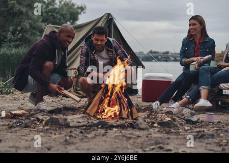 Leben voller Freundschaft. Gruppe junger Leute in Freizeitkleidung lächelt, während sie am Lagerfeuer eine Strandparty genießen Stockfoto