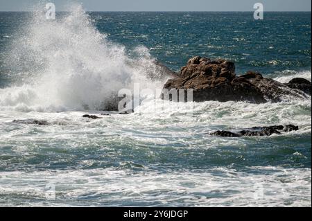 Mächtige Wellen krachen entlang der Küste auf Felsen und erzeugen einen nebeligen Sprühnebel. Stockfoto