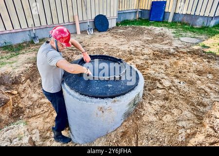 Der Arbeiter platziert den Stützring für die Mannlochabdeckung auf dem Klärgrubenring aus Beton. Stockfoto