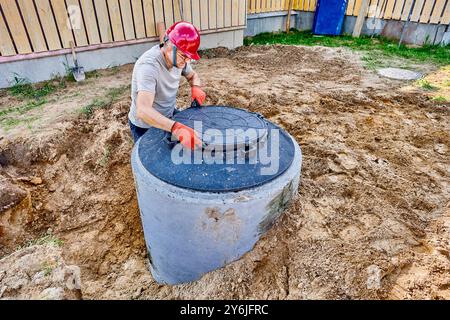 Ein Techniker installiert eine Mannlochabdeckung oder einen Klärtankdeckel auf Beton Stockfoto